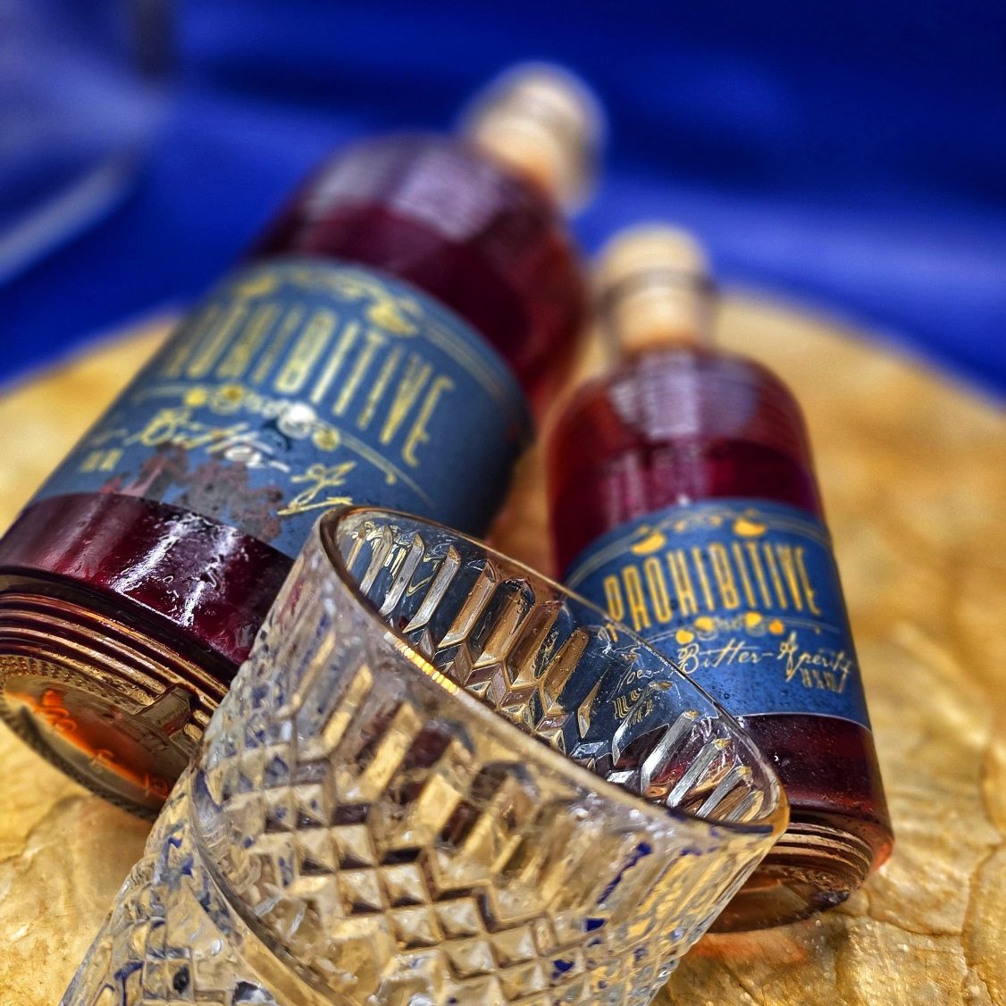 Prohibitive - Sloe Bitter Aperitif Zwei Flaschen alkoholischer Getränke und ein dekoratives Glas auf goldenem Hintergrund.